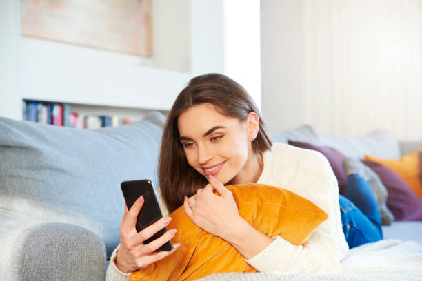 istock Smiling young woman text messaging while relaxing on sofa at home 1125941684
