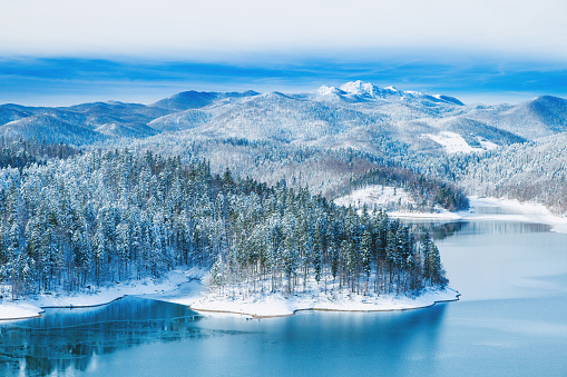 Croatian nature landscape, beautiful winter panorama of Lokvarsko lake and woods under snow in Gorski kotar and Risnjak mountain in background from drone
