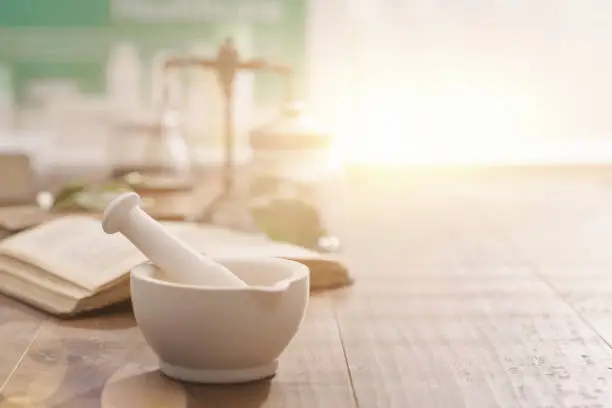 Photo of Mortar and pestle with pharmaceutical preparations's book and herbs on a wooden pharmacist table, traditional medicine and pharmacy concept