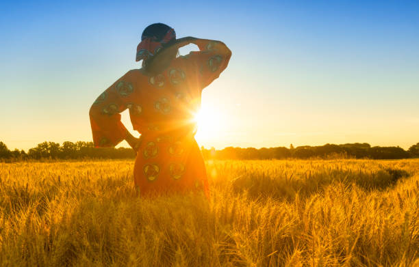femme africaine en vêtements traditionnels, debout, à la recherche, à la main des yeux, au champ des cultures de l’orge ou le blé au coucher du soleil ou au lever du soleil - traditional culture flash photos et images de collection