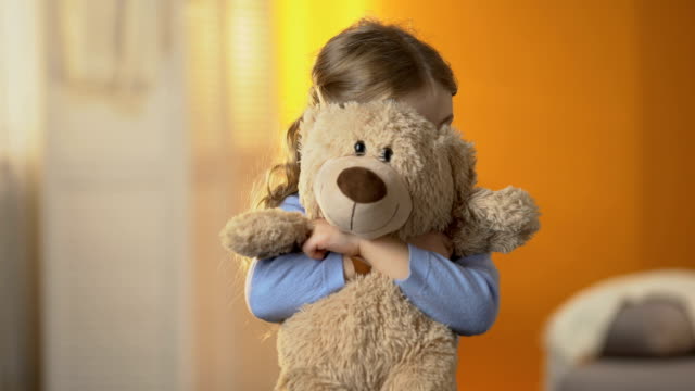 Preschool shy girl hiding behind teddy bear, childish psychological problems