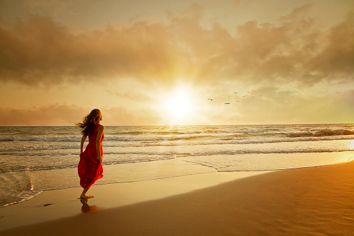 Attractive woman in beautiful dress on beach at sunset or sunrise. Freedom Concept.