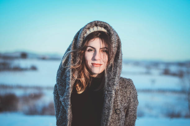 a beautiful young woman with a hood posing in the snow covered mountains. Winter Fashion/editorial style image with white accented makeup