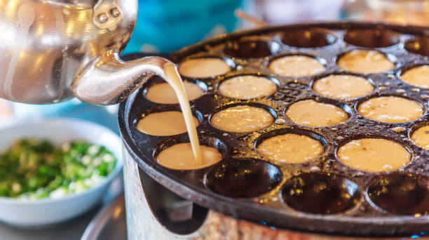 istock Khanom Khrok (coconut rice pancake), Traditional Thai Pudding Pancake Dessert, prepared by mixing rice flour, sugar, and coconut milk to form dough cooked in heating mantle (hot indented frying pan) 1125970588