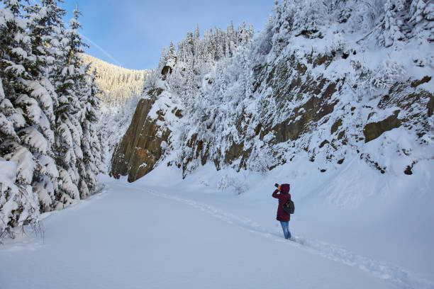 Tourist woman with backpack and camera taking landscapes photos in the winter