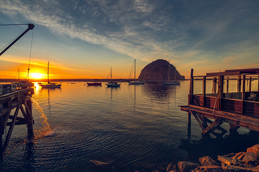 Beautiful sunset over the ocean, sailing boats, big rock, blue water, and colorful sky, Morro Bay harbor, California