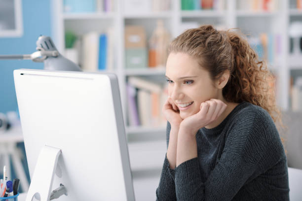 istock Young smiling beautiful woman using a computer in the office and connecting online, she is watching videos and films 1125981843