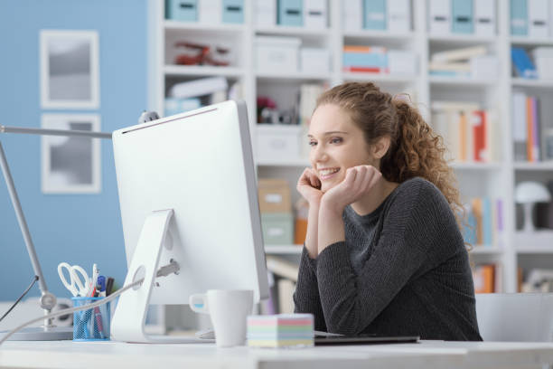 istock Young smiling beautiful woman using a computer in the office and connecting online, she is watching videos and films 1125982041
