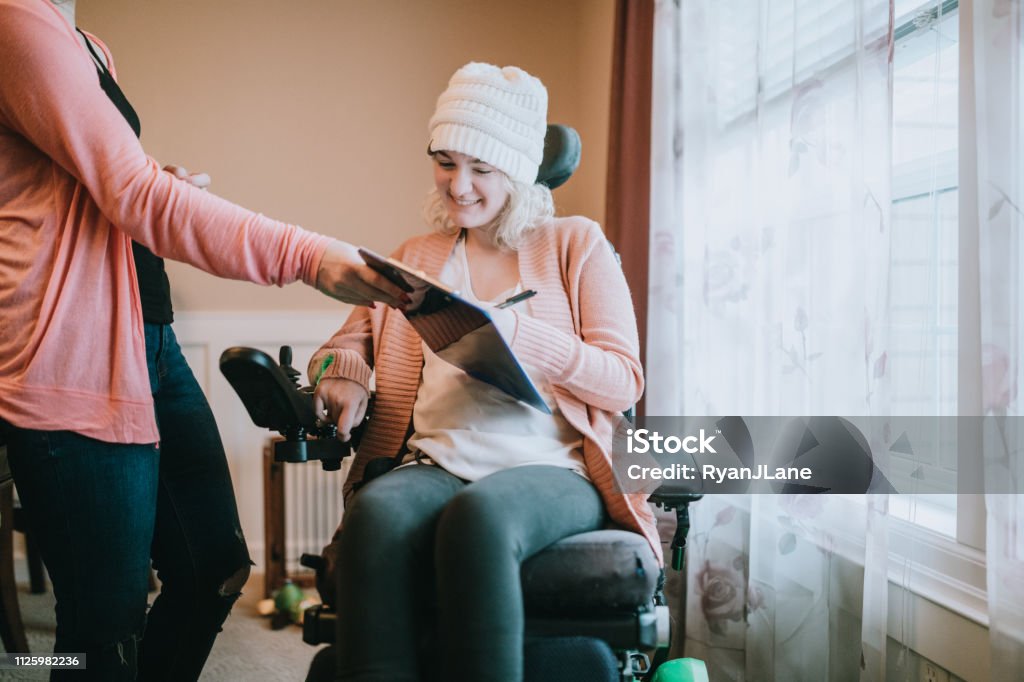 Fröhliche junge Frau im Rollstuhl Unterzeichnung zu Hause Papiere - Lizenzfrei Rollstuhl Stock-Foto