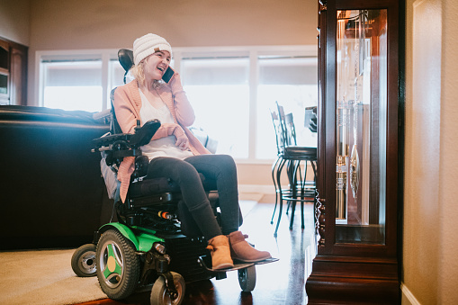 An independent young adult woman with cerebral palsy going about some of her daily routines at home.  She smiles while talking to a friend on her phone.