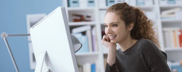 Young smiling beautiful woman using a computer in the office and connecting online, she is watching videos and films