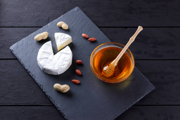 istock Camembert and honey on black slate board. Soft cheese with mold and peanuts on black background. Cheese and nuts on stone board 1125991952
