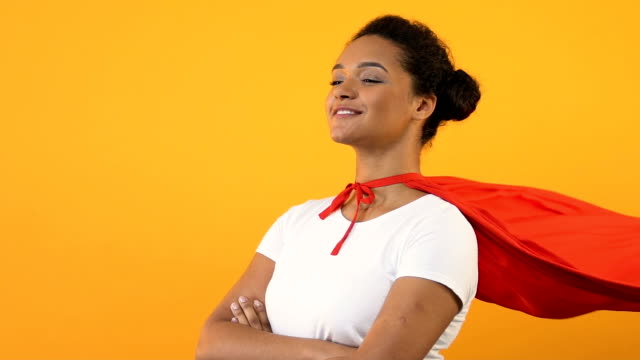 Self-confident afro-american woman with crossed hands in red cape, super hero