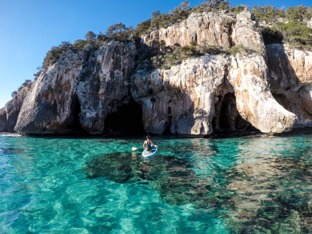 Woman stand up paddling towards cliffs and caves stock photo