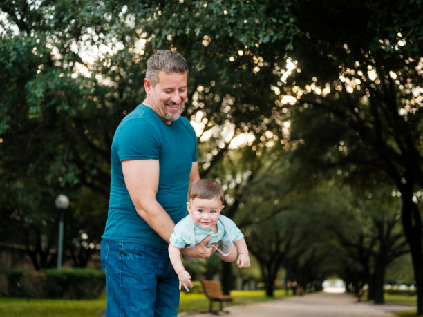 A mexican father carrying baby boy like an airplane and playing outdoors.