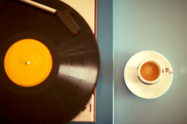 A vinyl record being played on a vintage turntable and a single cup of espresso.