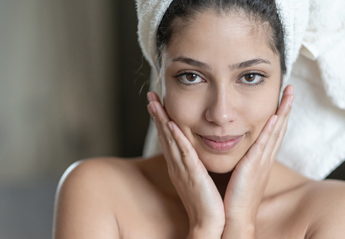 Beauty portrait of a Latin American woman in the bathroom looking at the camera smiling and wearing a towel on her head - beauty concepts