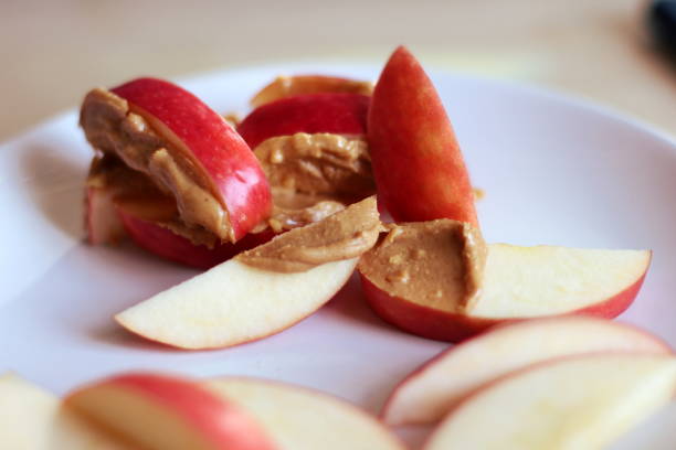 Apple Slices with Peanut Butter Sliced red apple with crunchy peanut butter spread on top. Served on a white plate with a pale background. peanutbutter stock pictures, royalty-free photos & images