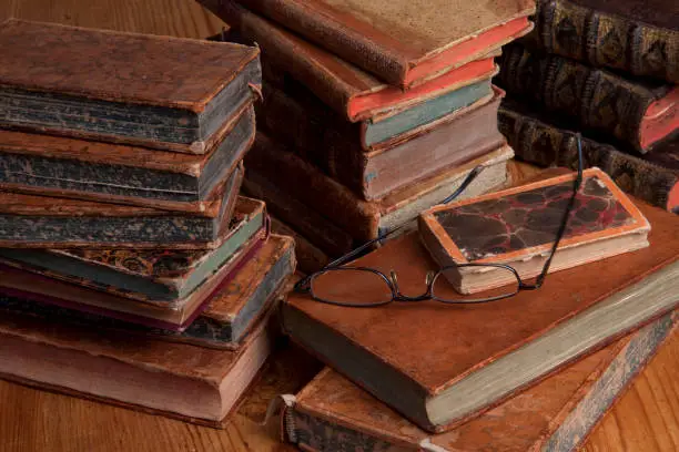 Vintage books are stacked with a pair of reading glasses on top.