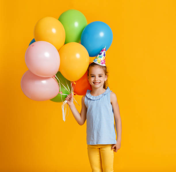 herzlichen glückwunsch zum geburtstag! kind mädchen mit luftballons auf gelbem hintergrund - balloon child people color image stock-fotos und bilder
