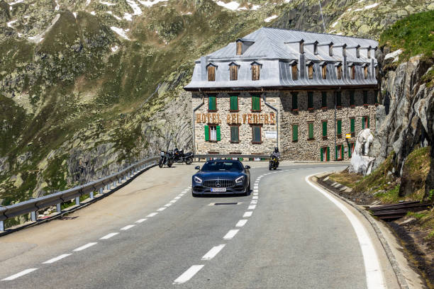 Sport car and motorcyclist passing Hotel Belvedere on the way up to Furka Pass, a spectacular road featured in James Bond Goldfinger movie, Switzerland Sportcar and motorcyclist passing Hotel Belvedere on the way up to Furka Pass, a spectacular road featured in James Bond Goldfinger movie. Furka Pass, Valais, Switzerland, July 2018 furka pass photos stock pictures, royalty-free photos & images