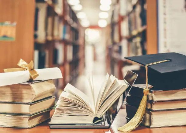 Photo of E-learning class and internet online education success with IT computer laptop, graduation hat, academic cap, mortarboard and degree certificate on books in class or library study room