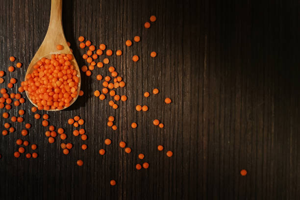 Orange lentils in veneer. On a wooden dark background I am sprayed in a spoon