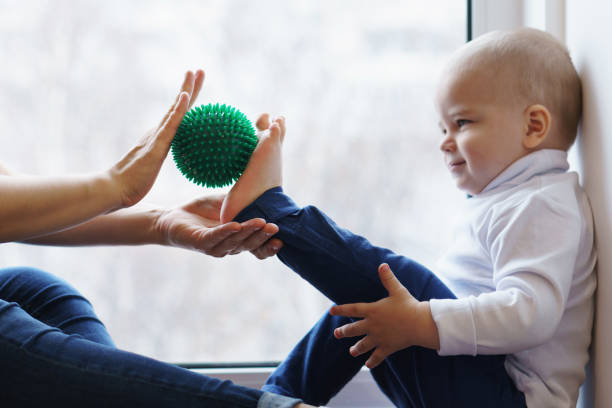 Mother doing foot massage son Mother makes foot massage to her son. She is holding massage ball. Little boy is smiling, he is tickled. Family care. Prevention of flatfoot pes planus stock pictures, royalty-free photos & images