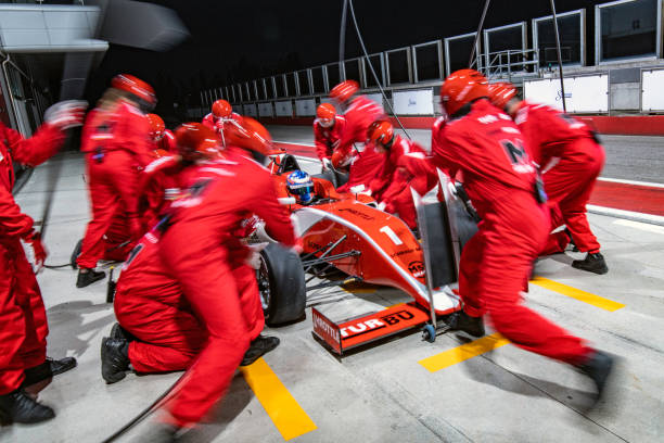 Pit stop crew servicing a formula race car Pit stop crew making quick repairs and changing tires on red a formula car. pitstop stock pictures, royalty-free photos & images