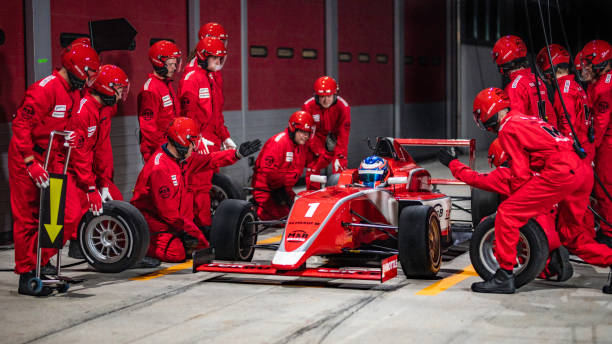 Pit crew preparing to change tires on formula car Pit crew in red uniforms preparing to service a red formula race car and change it's tires. pitstop stock pictures, royalty-free photos & images