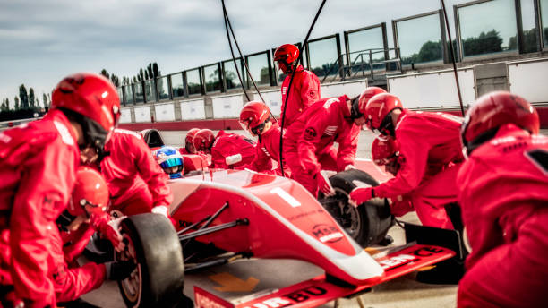 Mechanics changing tires on a formula during a pit stop Pit crew in red uniforms changing tires on a single-seater car during it's stop at a pit stop. pitstop stock pictures, royalty-free photos & images