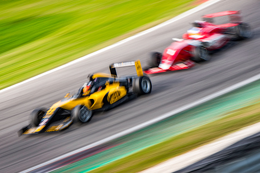 Blurred tilted photo of two formula race cars driving very close to each other.