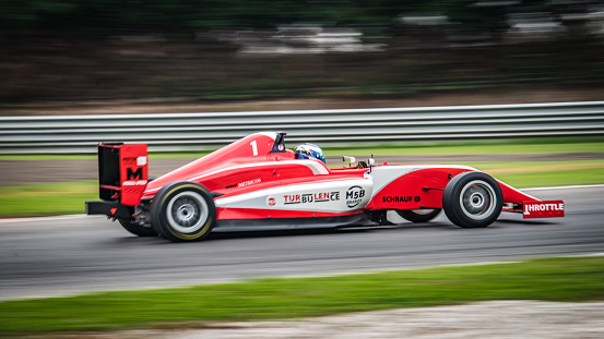 Panning side view photo of a red formula car driving fast.