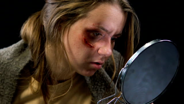Woman looking at wound in mirror, feels desperate to stop domestic violence