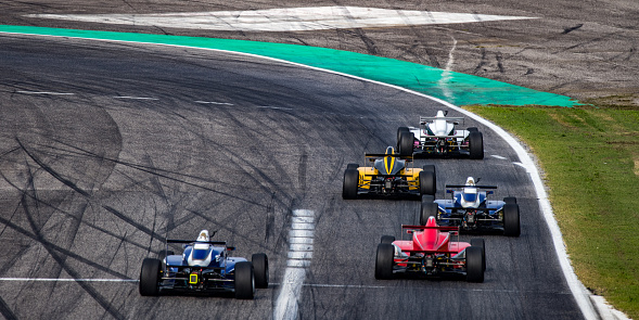 Rear view of five formula race cars on the track about to turn.