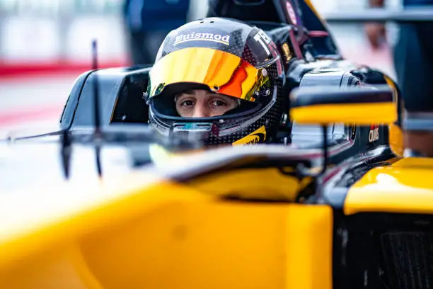 Portrait of a race car driver with a raised visor in his formula car looking at the camera.