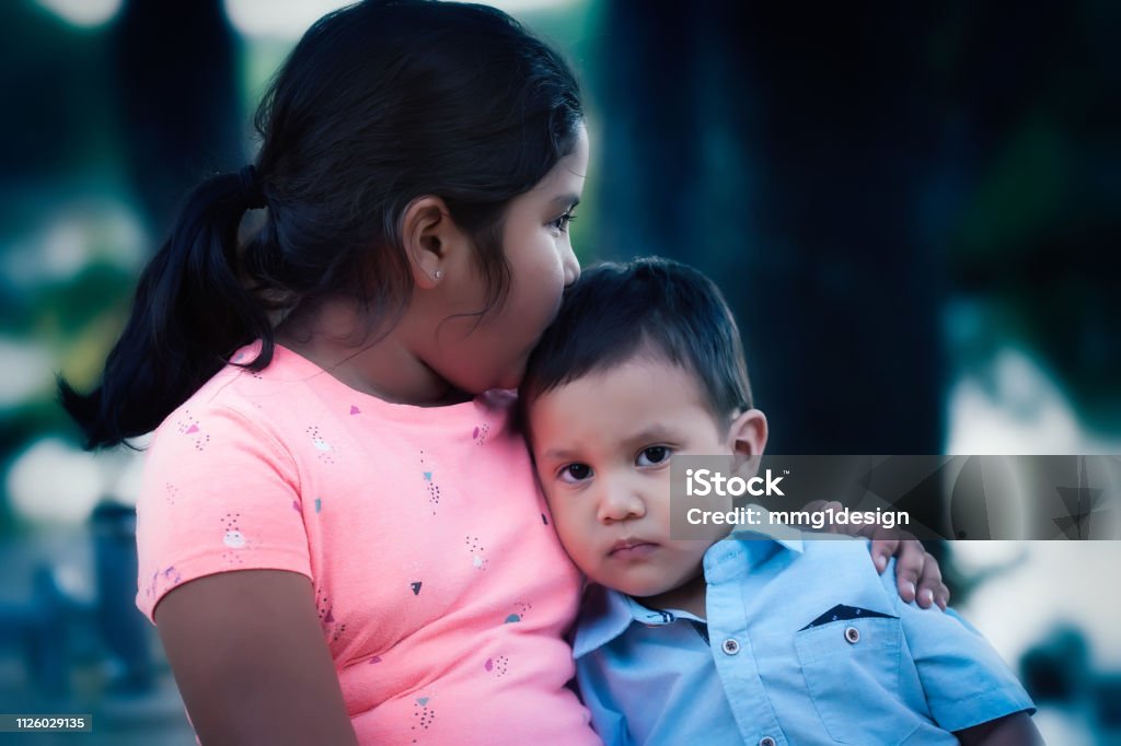 An emotionally hurt young boy leaning on her older sister and being comforted by her kiss and support. Child Stock Photo