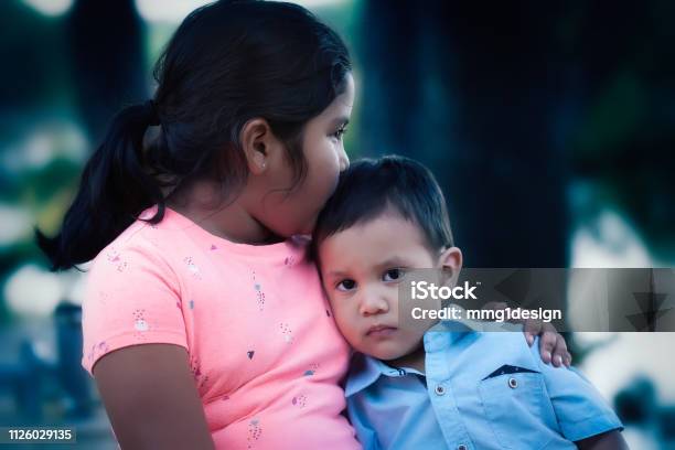 An Emotionally Hurt Young Boy Leaning On Her Older Sister And Being Comforted By Her Kiss And Support Stock Photo - Download Image Now