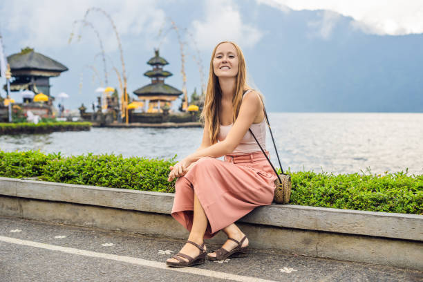 giovane viaggiatrice sullo sfondo di pura ulun danu bratan, bali. tempio indù circondato da fiori sul lago bratan, bali. grande tempio dell'acqua sciita a bali, indonesia. tempio indù - 11091 foto e immagini stock