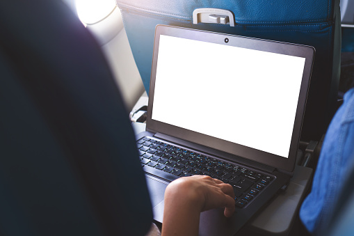 Rear view of business person working on laptop during the flight, blank screen of laptop