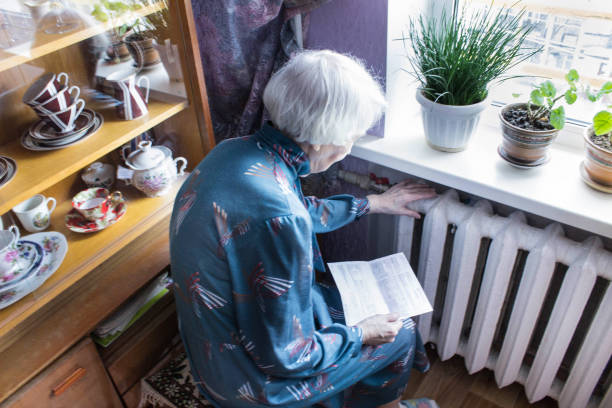 Woman holding cash in front of heating radiator. Payment for heating in winter. Selective focus. The senior woman holding gas bill in front of heating radiator. Payment for heating in winter. home heating stock pictures, royalty-free photos & images