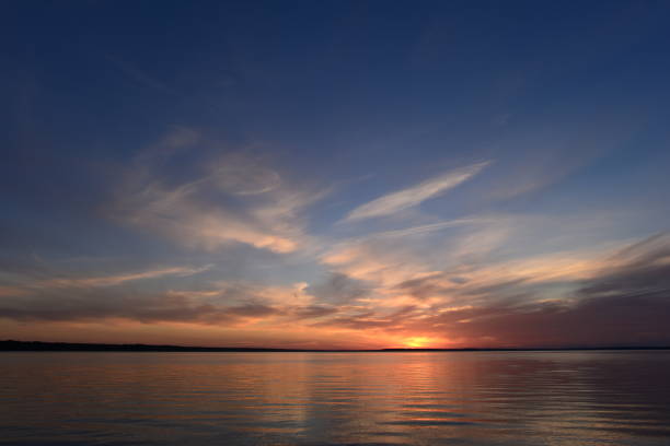 istock Sunlight in the clouds on the horizon under a clear blue sky at sunset over the glowing quiet surface of the lake water. 1126042029