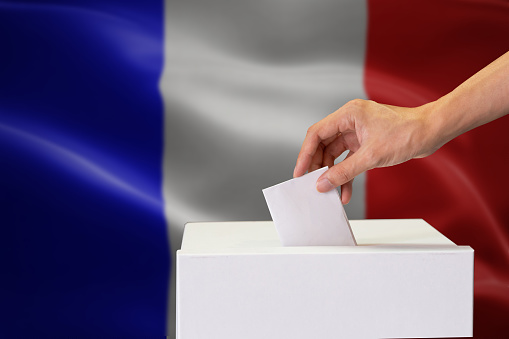 Close-up of human hand casting and inserting a vote and choosing and making a decision what he wants in polling box with France flag blended in background