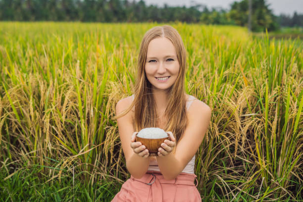 una donna tiene una tazza di riso bollito in una tazza di legno sullo sfondo di una risaia matura - 11262 foto e immagini stock