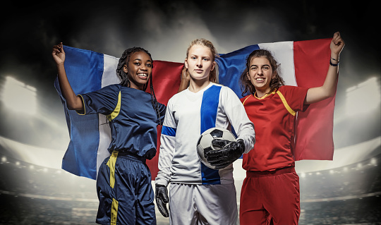 Three mixed race Female Football Players with a Soccer Ball in front of Stadium Lights