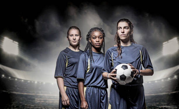 Three Female Soccer Players Three mixed race Female Football Players with a Soccer Ball in front of Stadium Lights soccer team captain stock pictures, royalty-free photos & images