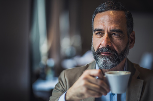 Portrait of a bearded senior man drinking coffee in a cafe.