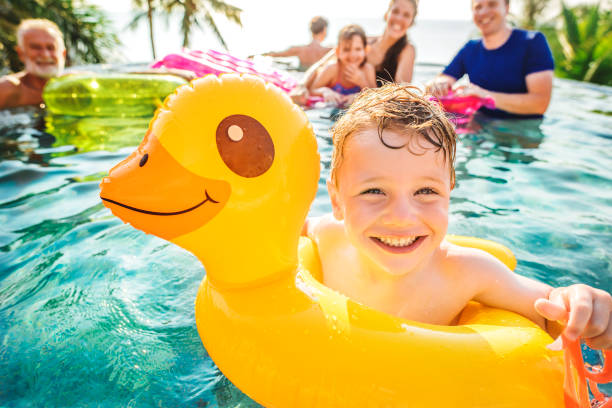 мальчик, плавающий в бассейне с семьей - family vacation стоковые фото и изображения