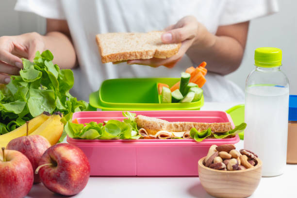 istock Mother preparing school lunch box set, Ham cheese sandwich with cucumber, carrot and nuts, fruits and vegetable in box. Healthy and Diet food. 1126058954