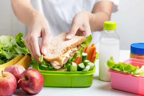 matka przygotowuje zestaw szkolnych pudełek na lunch, kanapkę z serem szynka z ogórkiem, marchewką i orzechami, owocami i warzywami w pudełku. zdrowa i dietetyczne jedzenie. - lunch box lunch packed lunch school lunch zdjęcia i obrazy z banku zdjęć